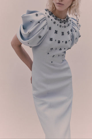 Woman wearing a light blue dress with intricate detailing on a plain background